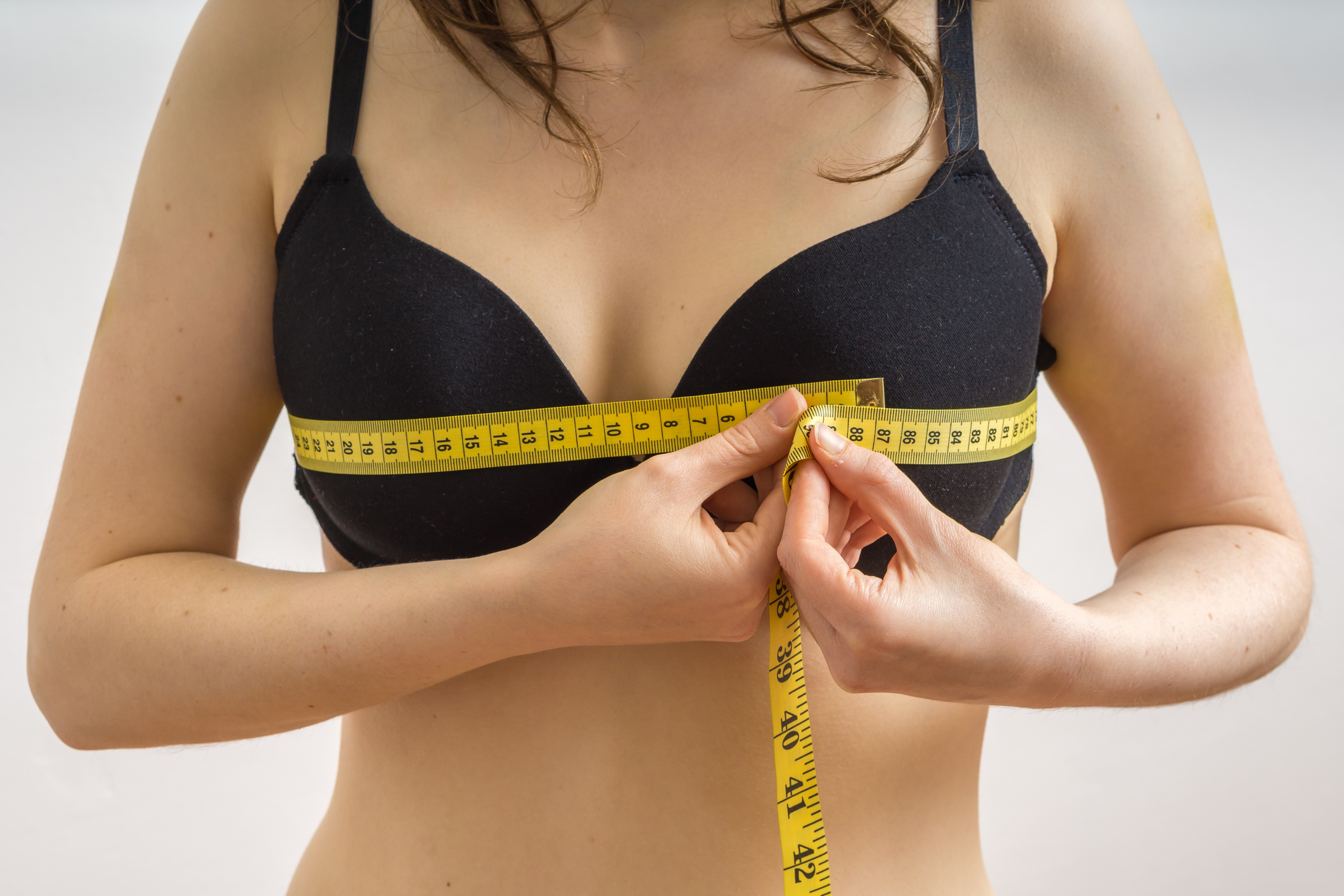 Image of closeup midsection of a young woman measuring breasts